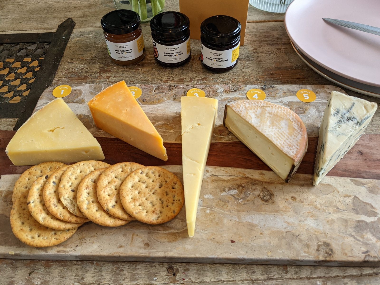 A cheeseboard with five cheeses, crackers and preserves