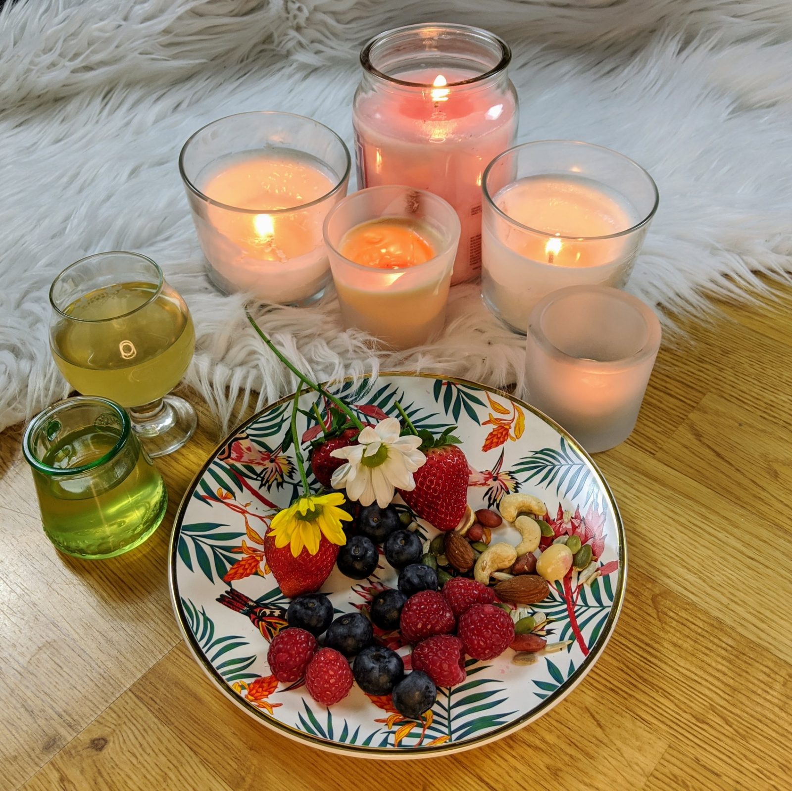 Candles glowing beside a plate of berries, nuts and flowers