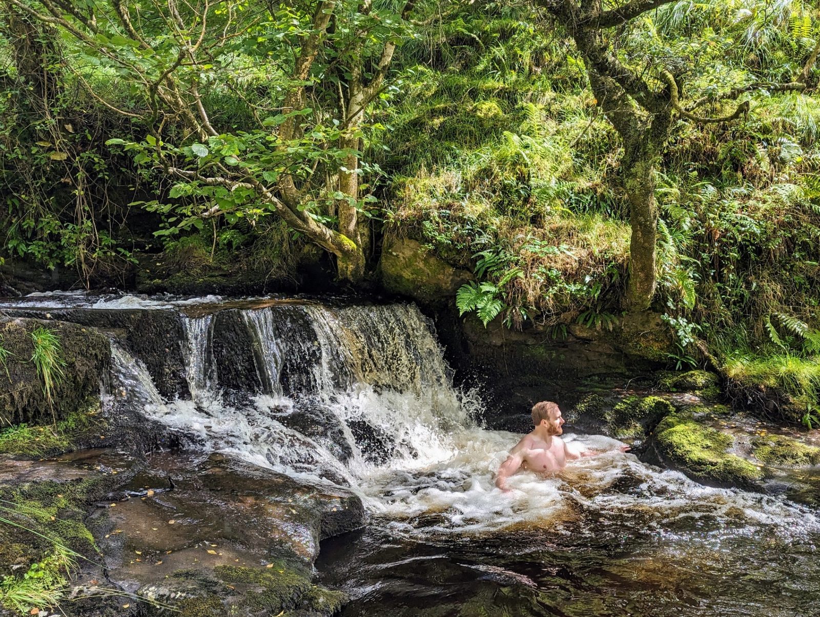 A man bathing in a small woodland waterfall pool