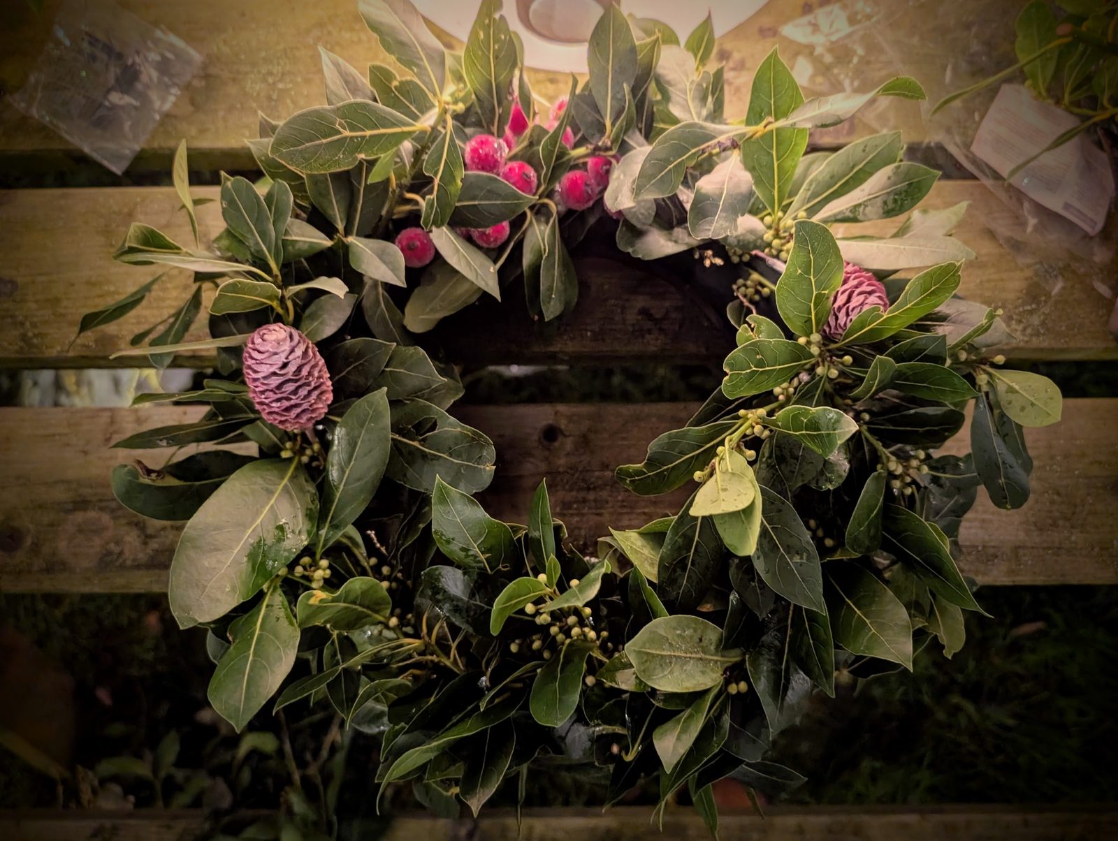 A bay leaf wreath with pink berries and cones on rustic wood