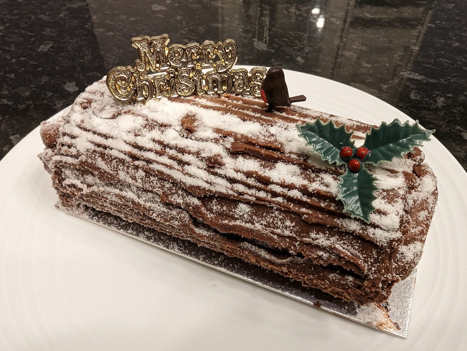 A chocolate yule log dusted with icing sugar, topped with a robin and holly